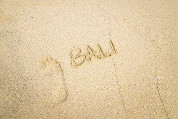 The word BALI is writting on the sand with footprints and wave. drawing on the sand. writing with sands on the beach. 