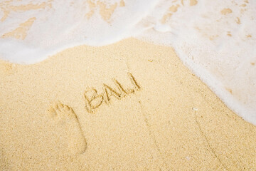The word BALI is writting on the sand with footprints and wave. drawing on the sand. writing with sands on the beach. 
