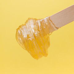 Wooden spatula with liquid sugar paste for depilation on a yellow background. Epilation, depilation, hair removal, beauty.