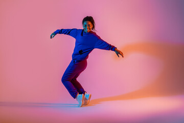 Fototapeta na wymiar Street dance style. Happy black female hip-hop dancer dancing in neon pink lights, studio background, free space