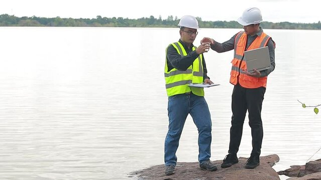 Environmental two engineers work at water source to check for contaminants in water sources and analyzing water test results for reuse.World environment day concept.