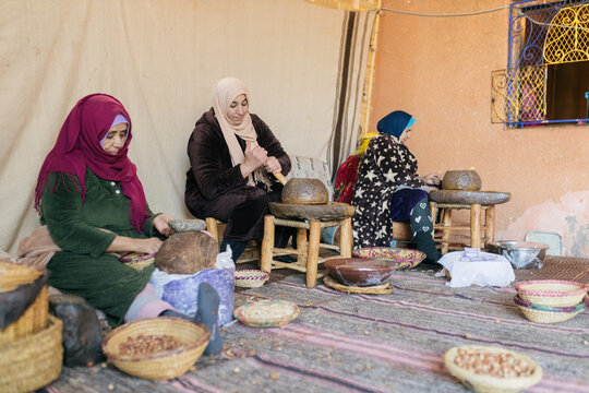 Three Arab women working sitting in a cooperative grinding argan nuts to extract oil