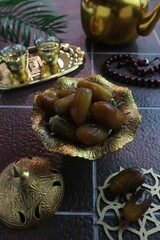 serving of dates in a gold bowl against a background of glasses on a gold tray and teapot