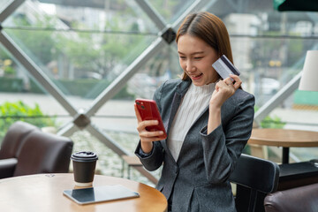 Young asian businesswoman beautiful female lady sitting in a cafe and confidently doing online payment transaction using her mobile phone digital banking app and credit card