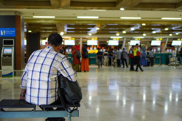 Airport traveler waiting for his turn at the check-in counter. Lonely traveler sitting in front of the check-in desk
