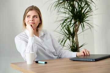 A young girl in a white shirt is sitting at the table. Online learning. Satisfaction from working on a business project.
