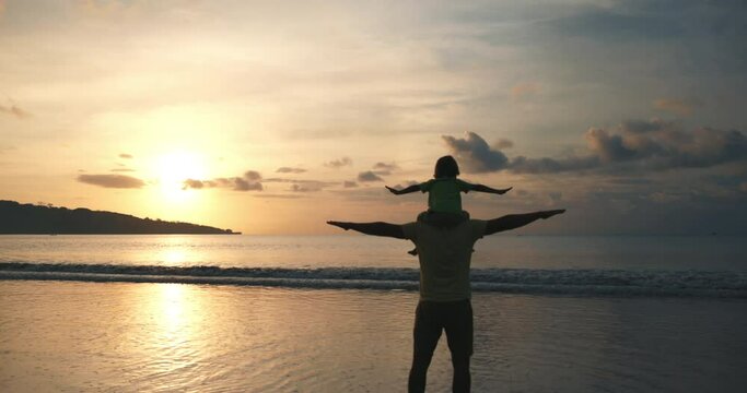 Silhouette of kid sitting on dad's neck and they spreading hands like bird wings