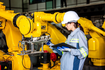 female engineer wearing a safety helmet walks inspecting the operation of the robot operating and operating the robotic arm in production efficiency in a factory.