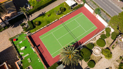 Aerial view of a hard tennis court. The field is green and the outlines red. The tennis court is in...