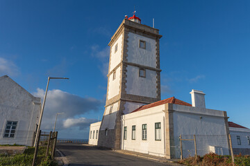 The building of the coastal lighthouse on a hill by the sea against the background of the blue sky