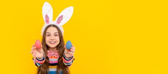 cheerful kid in bunny ears and bow tie hold easter eggs on yellow background. Easter child...