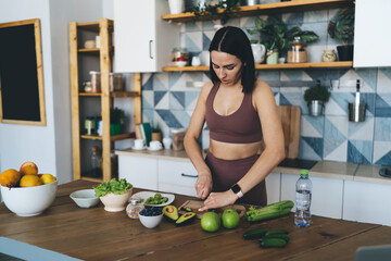 Focused woman standing in kitchen and cutting vegetables