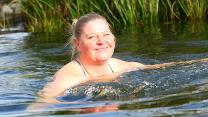 An elderly woman swims in a garden pond. Enjoying life during her vacations.
