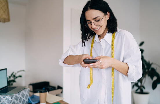 Cheerful young tailor taking photo on mobile phone in atelier
