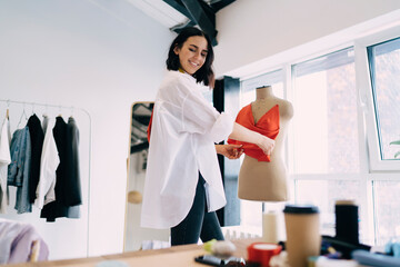 Smiling female tailor working on new clothes in atelier