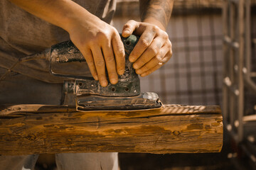 Craftsman's hands close up with old polishing machine on wooden logs. Working on wood with a special woodworking machine. Carpenter or engineer master working hard. Electric polisher, Orbital sander.