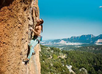 Strong muscular body man rock climber climbing on height vertical rock with rope on a mountains and...