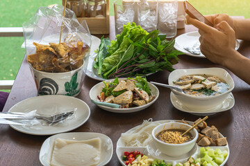 Spicy Vietnamese Pork Sausage Salad (Yum Moo Yor). Pork sausage spicy salad Thai and Vietnam food with other appetizing dishes and vegetables on wooden table with young man using mobile phone.