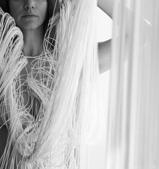 Fototapeta na wymiar body and part of portrait of a young gorgeous woman, attractive, sexy, naked, partially obscured by the white threads of a falling string curtain in beautiful shapes.