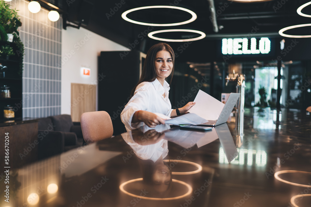 Poster smiling millennial worker with netbook and papers
