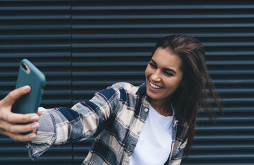 Happy young stylish lady taking selfie on mobile phone on street