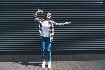 Cheerful young woman with smartphone dancing on street