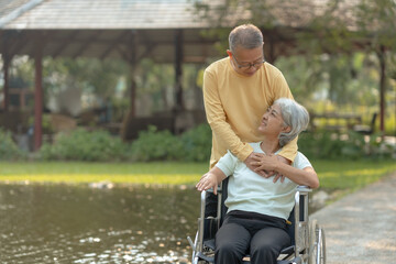 Fototapeta na wymiar Elderly couple. Asian couple giving love to each other smiling happily. Asian old husband caring and giving love to his wife in wheelchair.