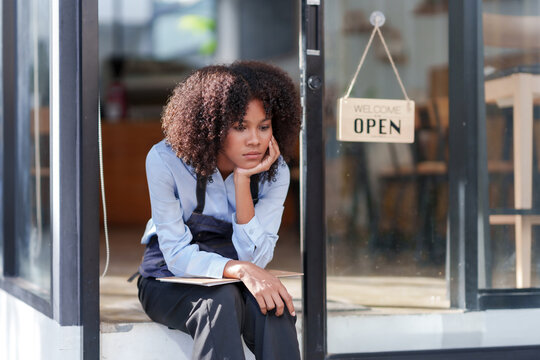 Female Shopkeeper Sitting Stressed Out At The Store Entrance Frustrated By The Economic Impact.