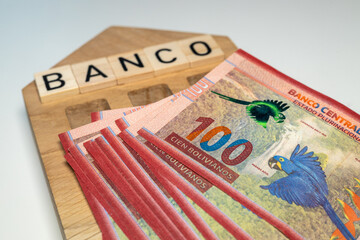 Bolivian money and the symbol of the bank of Colombia, a wooden miniature with the inscription banco, A lot of highest denomination banknotes, financial and business concept - obrazy, fototapety, plakaty