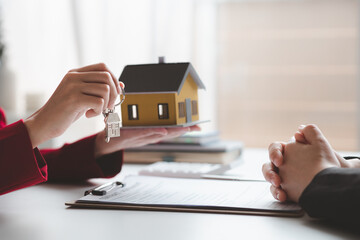 A home rental company employee is handing the house keys to a customer who has agreed to sign a...