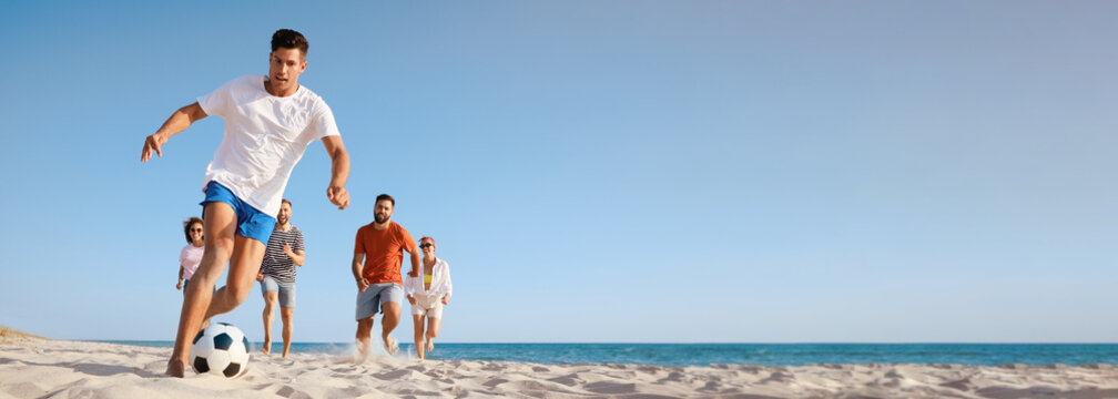 Group of friends playing football on sandy beach, low angle view. Banner design with space for text