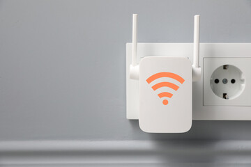 New modern repeater with Wi-Fi symbol plugged into socket on light grey wall, space for text
