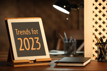 Trends For 2023 text on tablet display. Stationery and device on wooden table