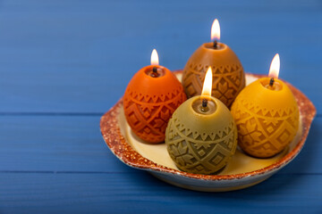 Easter candle eggs in a plate on a blue texture table with willow sprigs. Easter bunny.Happy easter.Easter candles and spring flower.Spring holiday concept.Copy space.Close-up.