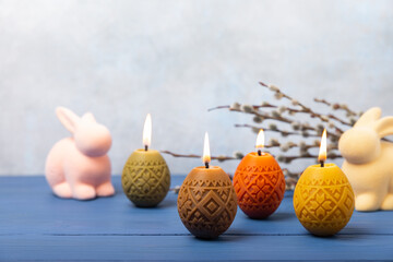 Easter candle eggs in a nest on a blue texture table with willow twigs. Easter bunny.Happy easter.Easter candles and spring flower.Spring holiday concept.Copy space.Close-up.