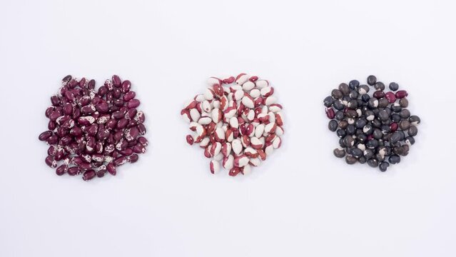 On white surface appear three piles of kidney beans of different colours, brown, red-white, black bean, crops, nutritious food, healthy diet, protein in vegetables, agriculture. Close up, 4K Ultra HD.