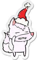 distressed sticker cartoon of a wolf showing teeth wearing santa hat