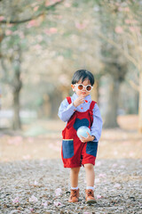 Asian kid have fun in the park near the blossom sakura tree background.Spring morning.