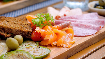 Eating smoked salmon with bread and veggies is a gourmet appetizer, delicious salted fish fillet and fresh ingredients. Fresh fillet is served on a rustic wooden board in restaurant.