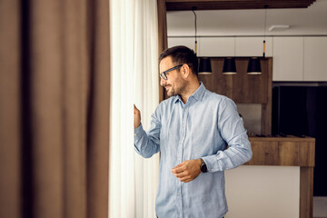 A man looking trough the curtain on the window from his home.