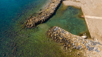 Aerial view of a long artificial reef near a small sandy cove near the sea. The beach is located in Santa Marinella, near Rome, Italy.