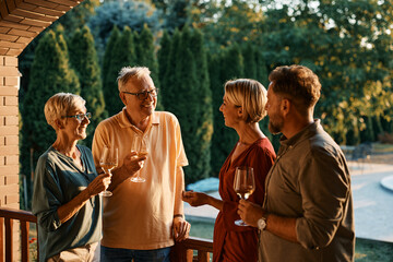 Happy couple enjoying in wine and conversation with their senior parents on patio at sunset.