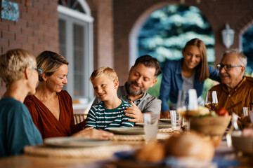 Happy kid enjoys with his extended family at dining table on patio.