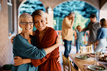 Happy woman hugs her senior mother during family gathering on patio.