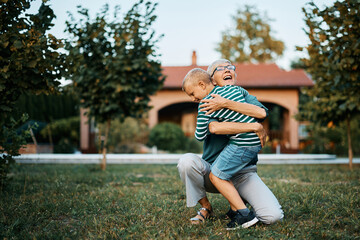 Cheerful grandmother and grandson embracing in backyard.