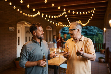 Happy man talks to his senior father while drinking beer together on patio.