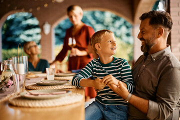 Happy father and son talk at dining table on patio.