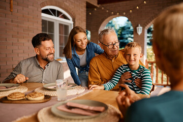 Happy multigeneration family talks while gathering for lunch at dining table on patio.