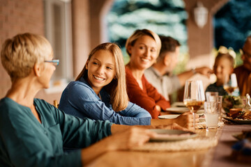 Happy teenage girl talks to her grandmother during family lunch on patio.
