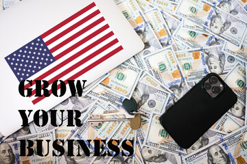 Grow your business concept. USA flag, dollar money with keys, laptop and phone background.